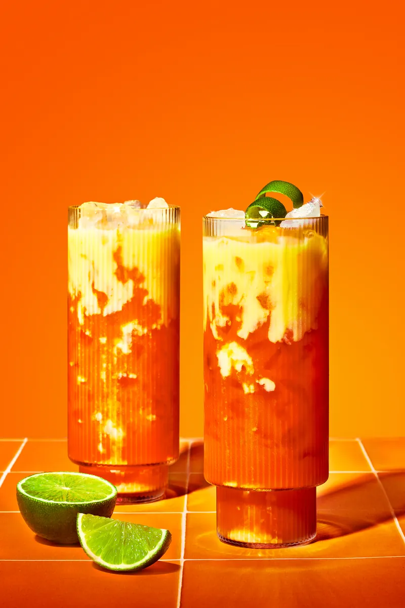 Two long drinks with lime against orange