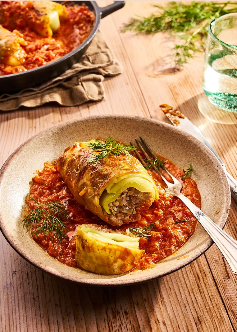 Kohlroulade in Tomatensoße auf hellem Holztisch