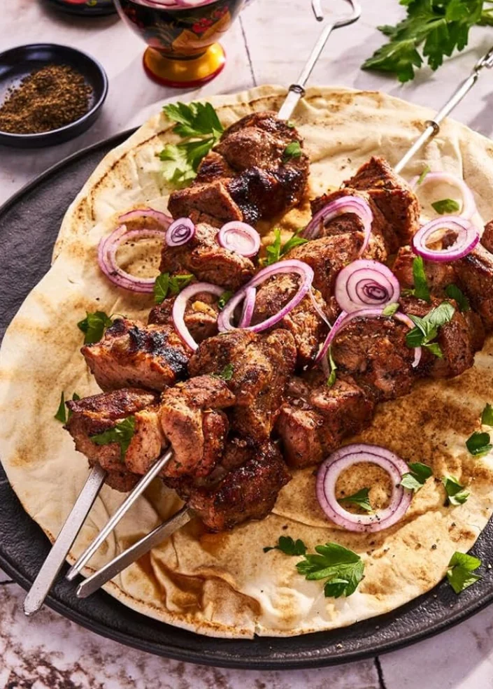 Schaschlik-Spieße auf Fladenbrot mit roten Zwiebeln und Kräutern