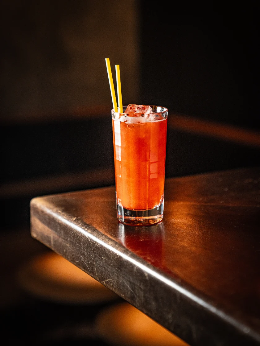 Roter Longdrink mit Strohhalmen auf einem Bartresen